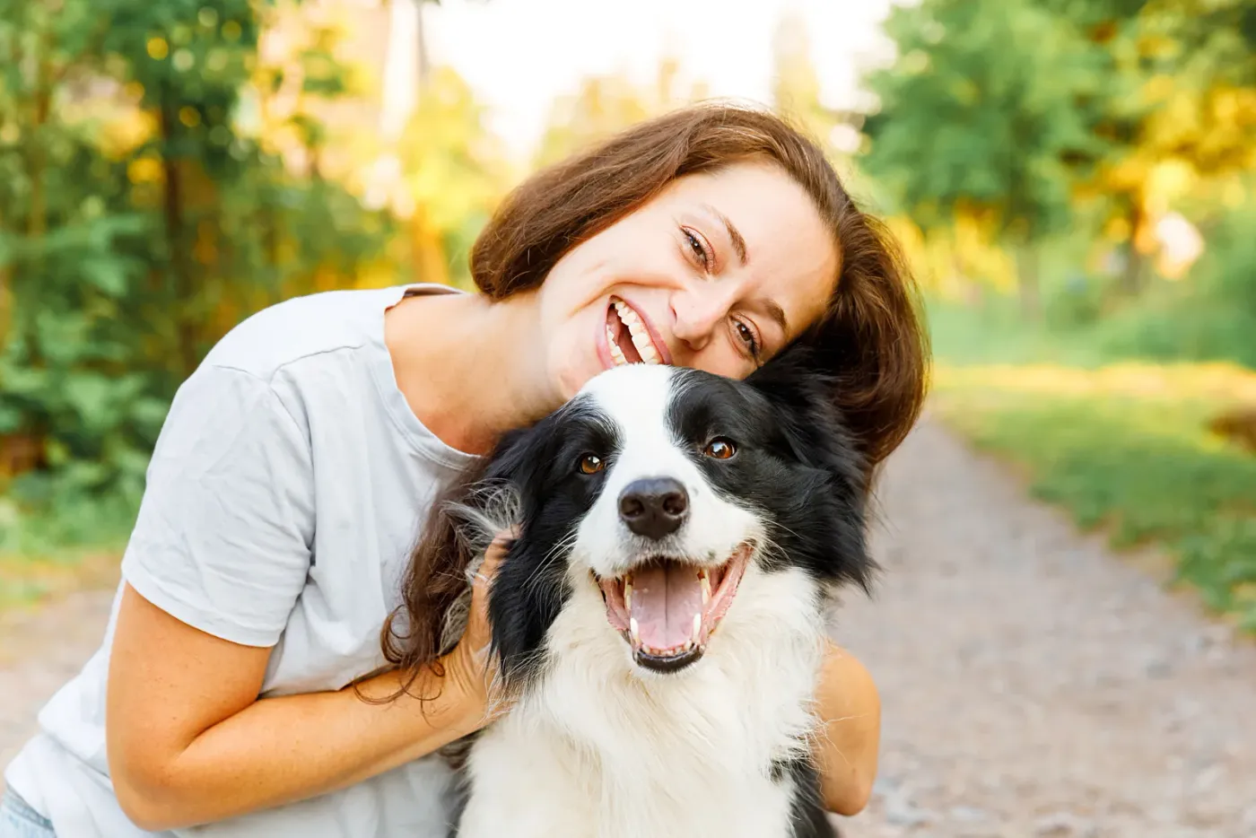 Smiling woman hugging a happy border collie on a walking path