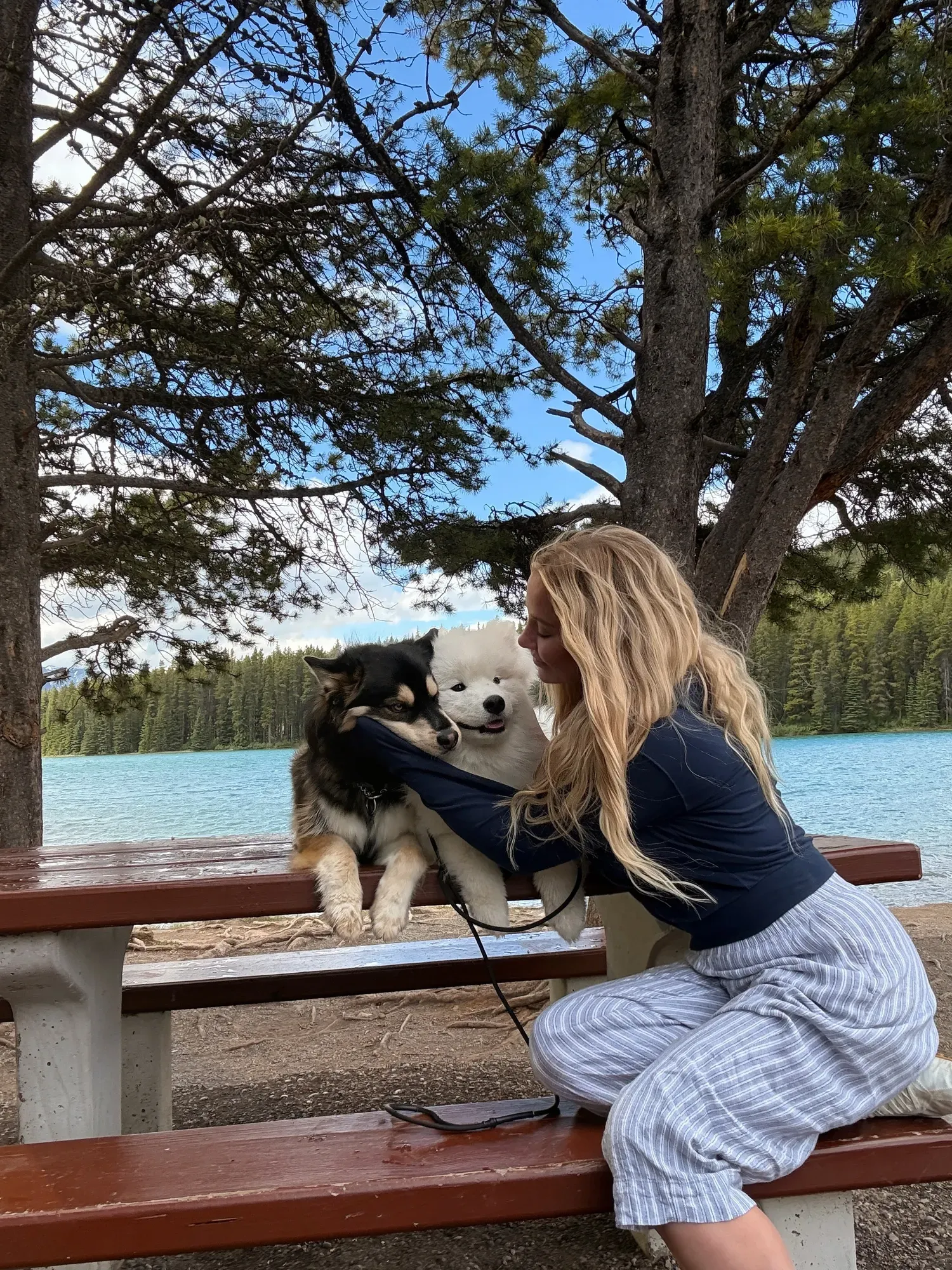 Kaitlin at a picnic table with two happy dogs by a turquoise mountain lake