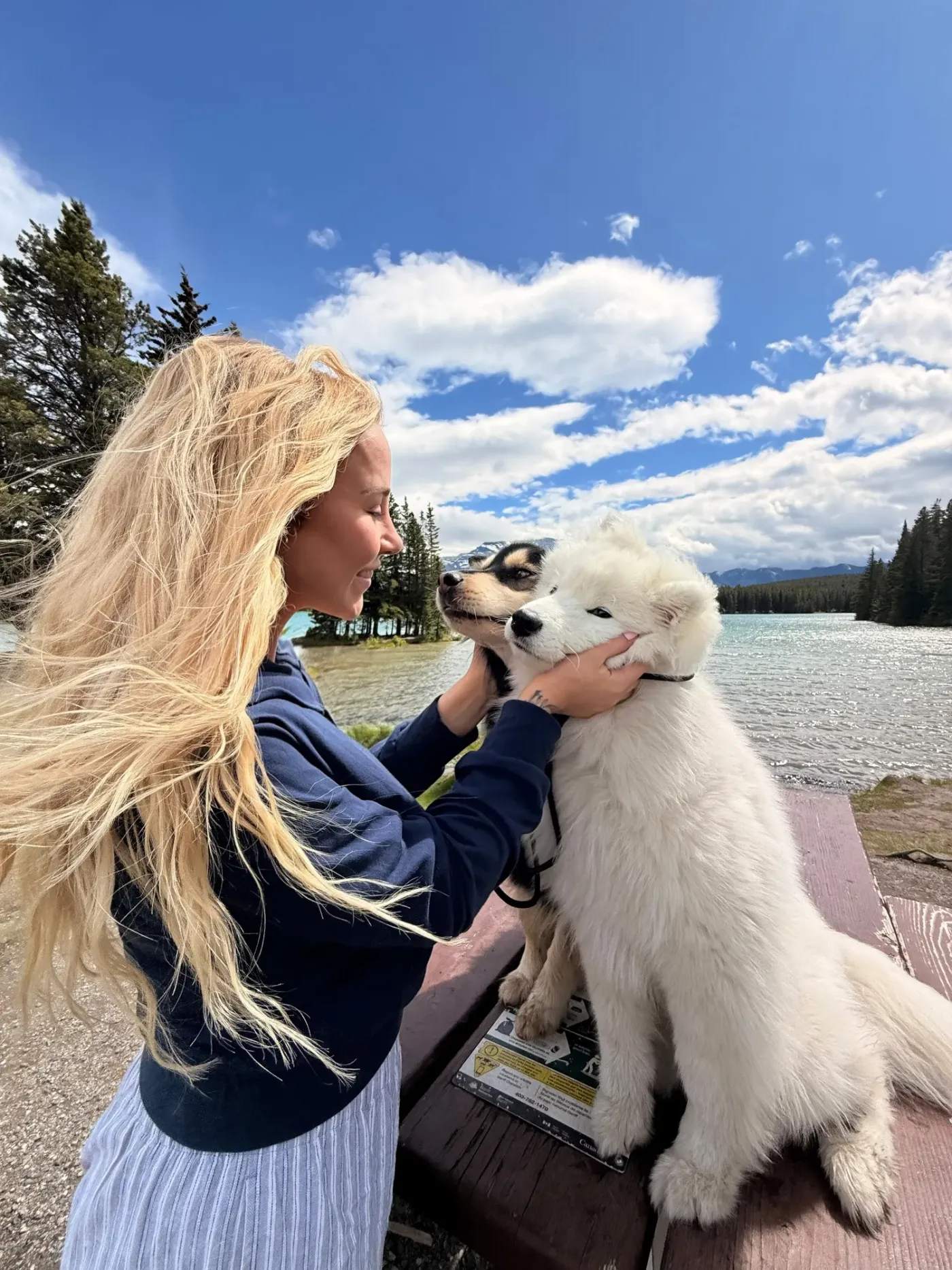 Kaitlin face to face with a happy white puppy under a blue summer sky
