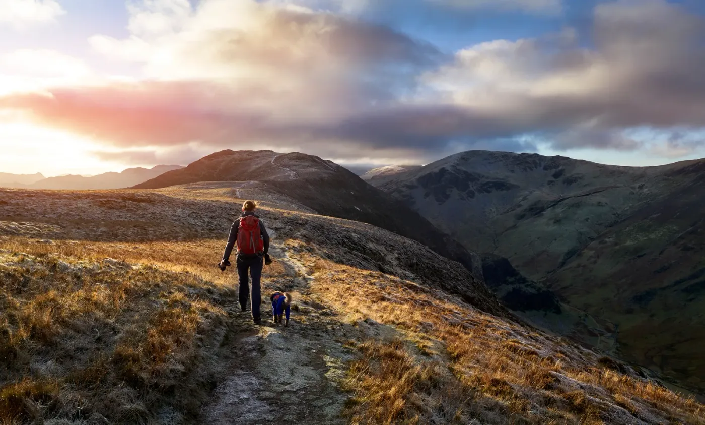 Hiker and dog on a ridge trail under a dramatic evening sky