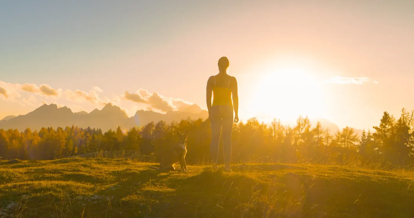 Woman and her dog on a hilltop at sunset with mountains on the horizon