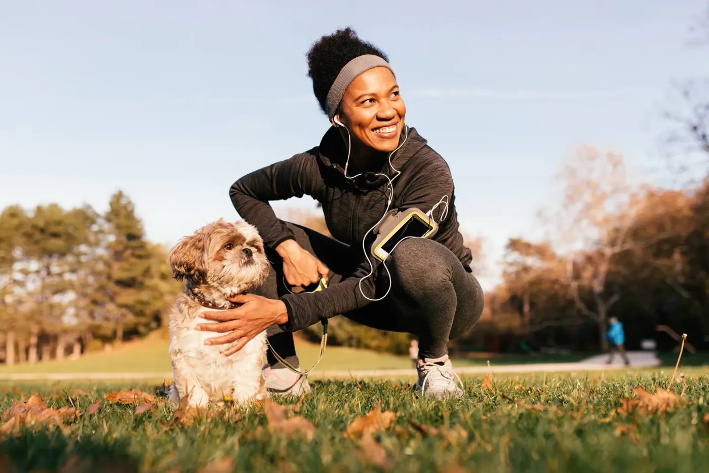 Woman crouching to pet a small dog on an autumn park lawn