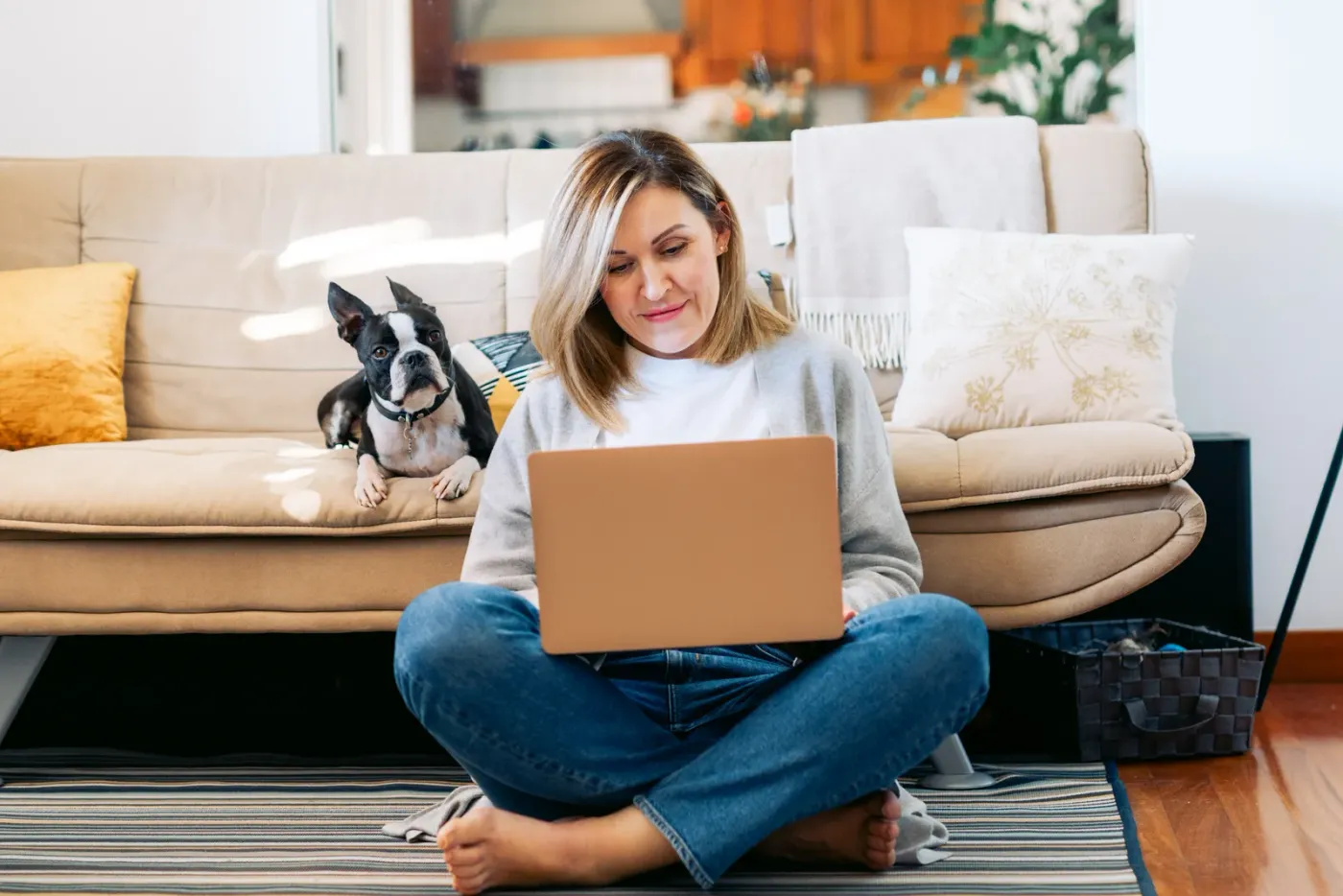 Woman working on a laptop with her Boston terrier on the couch